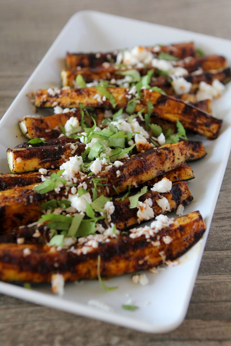 grilled plantains with feta cheese and herbs on a white serving platter