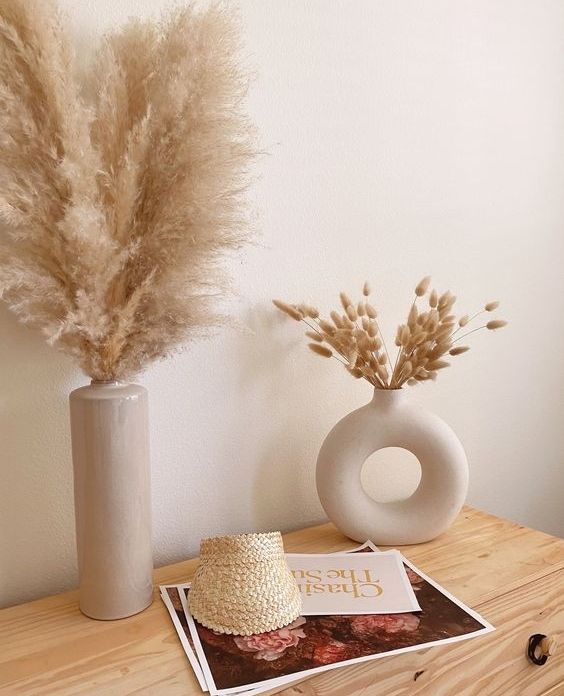 two vases with dry grass in them on a table next to a magazine and hat