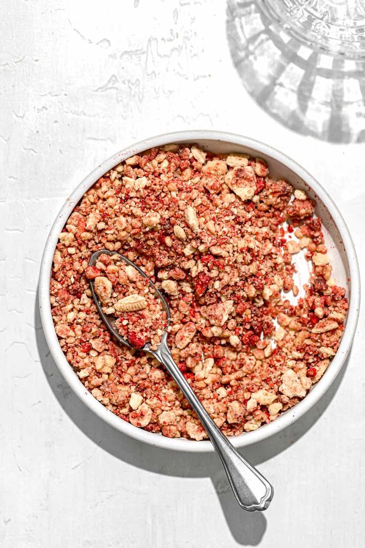 a white bowl filled with granola next to a metal spoon on top of a table