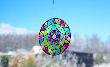 a colorful stained glass sun catcher hanging from a string in front of snow covered trees