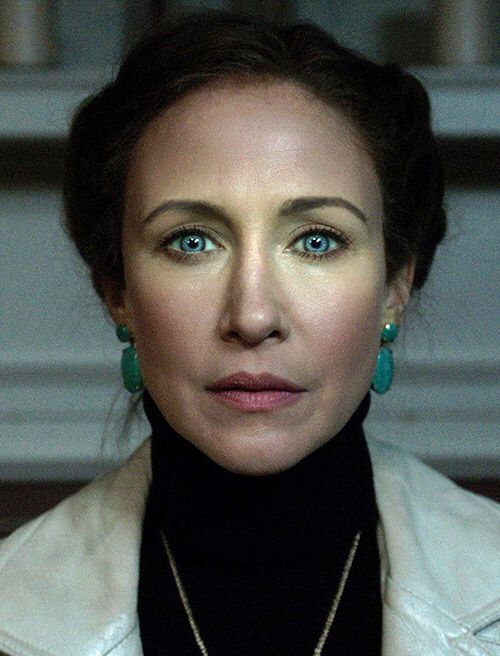 a woman with blue eyes wearing green earrings and a black turtle neck sweater is looking at the camera