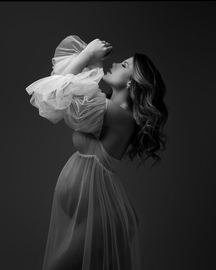 a woman in a white dress is posing with her hands behind her head and looking up into the air