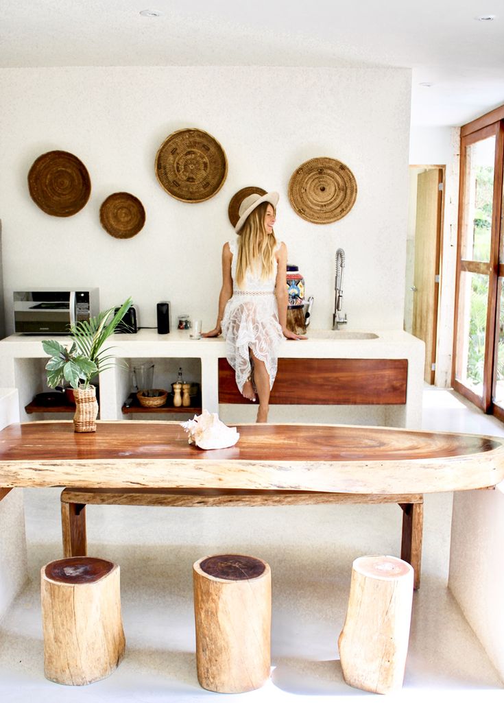 a woman standing in the kitchen next to a table with stools and potted plants on it