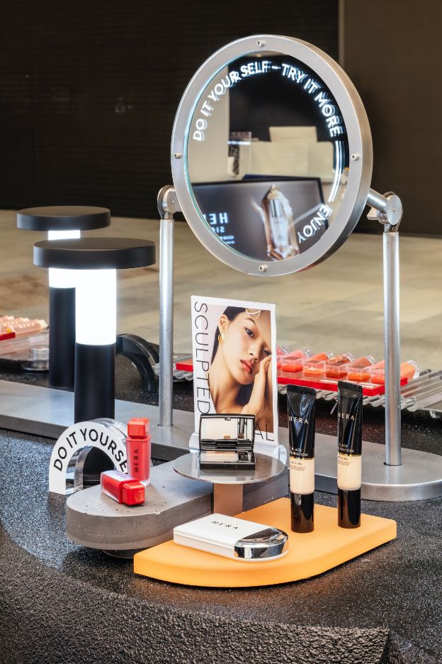 an assortment of beauty products on display in front of a mirror with the reflection of a woman's face