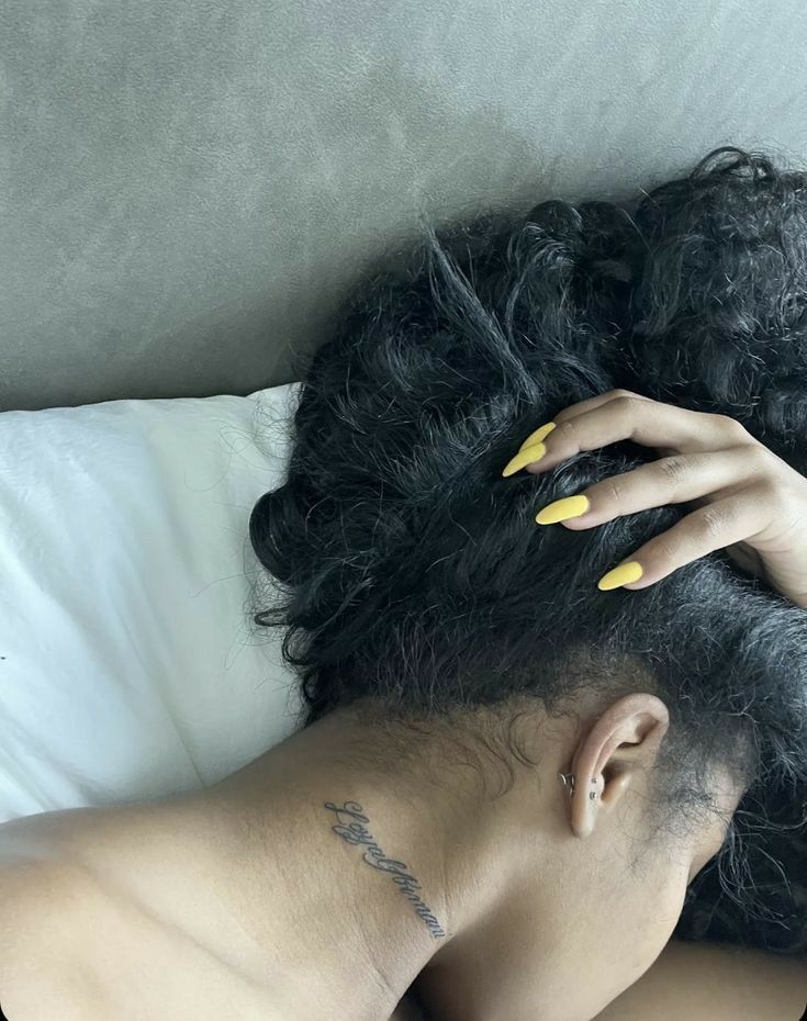 a woman with yellow nail polish laying on top of a bed next to her hair