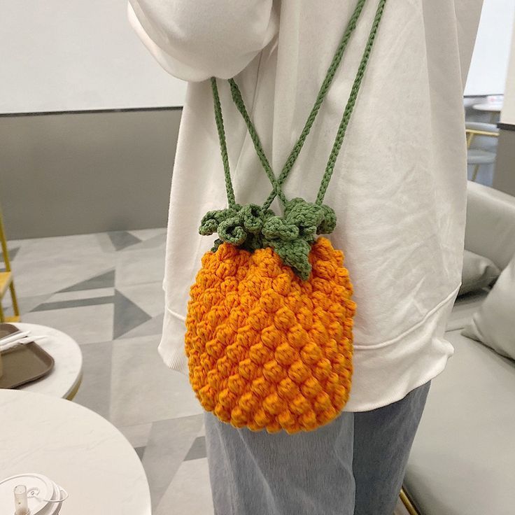 a person holding a crocheted orange purse on their shoulder and wearing a white t - shirt