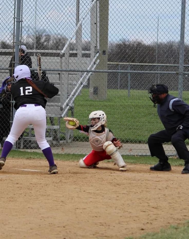 a batter, catcher and umpire during a baseball game on a dirt field in front of a chain link fence