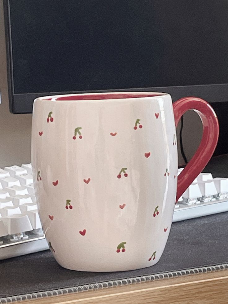 a red and white coffee mug sitting next to a computer keyboard