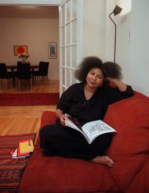 a woman sitting on top of a red couch next to a lamp and book case