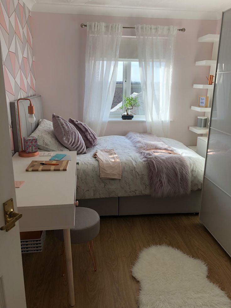 a small bedroom with a bed, desk and mirror in it's corner next to a window