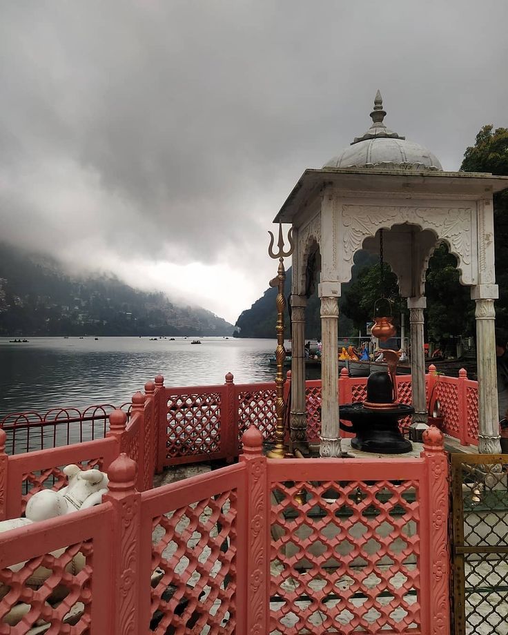 a gazebo sitting on the side of a body of water with mountains in the background