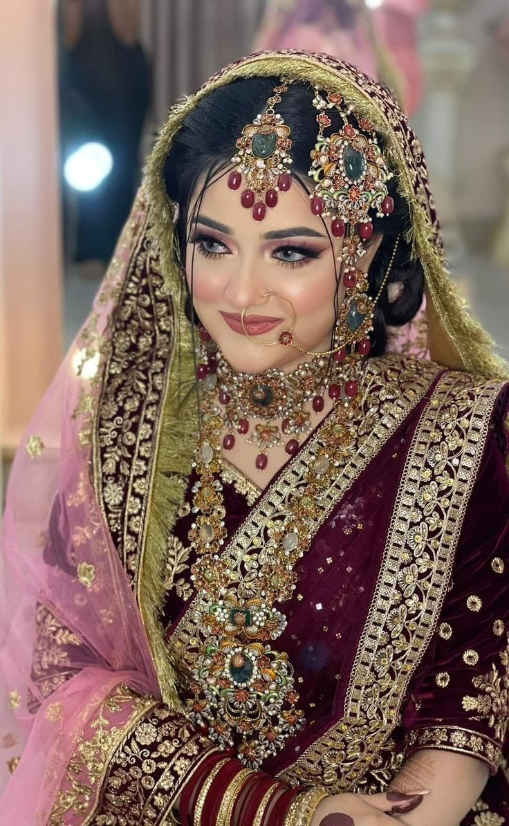 a woman in a red and gold bridal outfit with jewelry on her head, sitting down