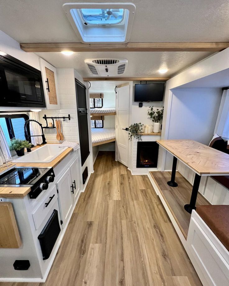 the interior of an rv with wood flooring and white walls, windows, and cabinets