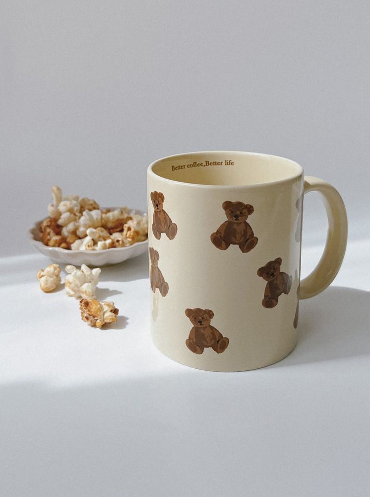 a coffee mug with teddy bears on it next to a bowl of popcorn