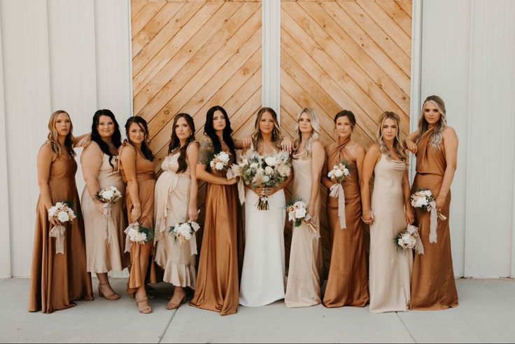 a group of women standing next to each other in front of a wooden wall holding bouquets