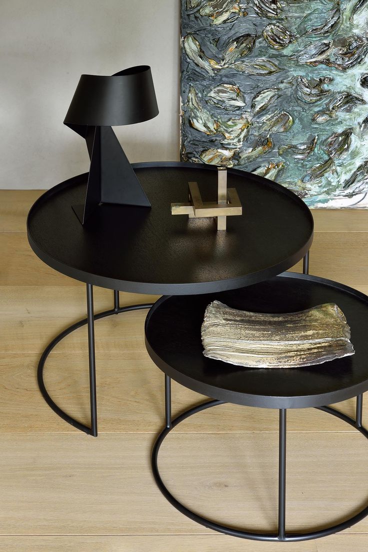 two round tables with black metal bases on wooden floor next to wall and painting in background