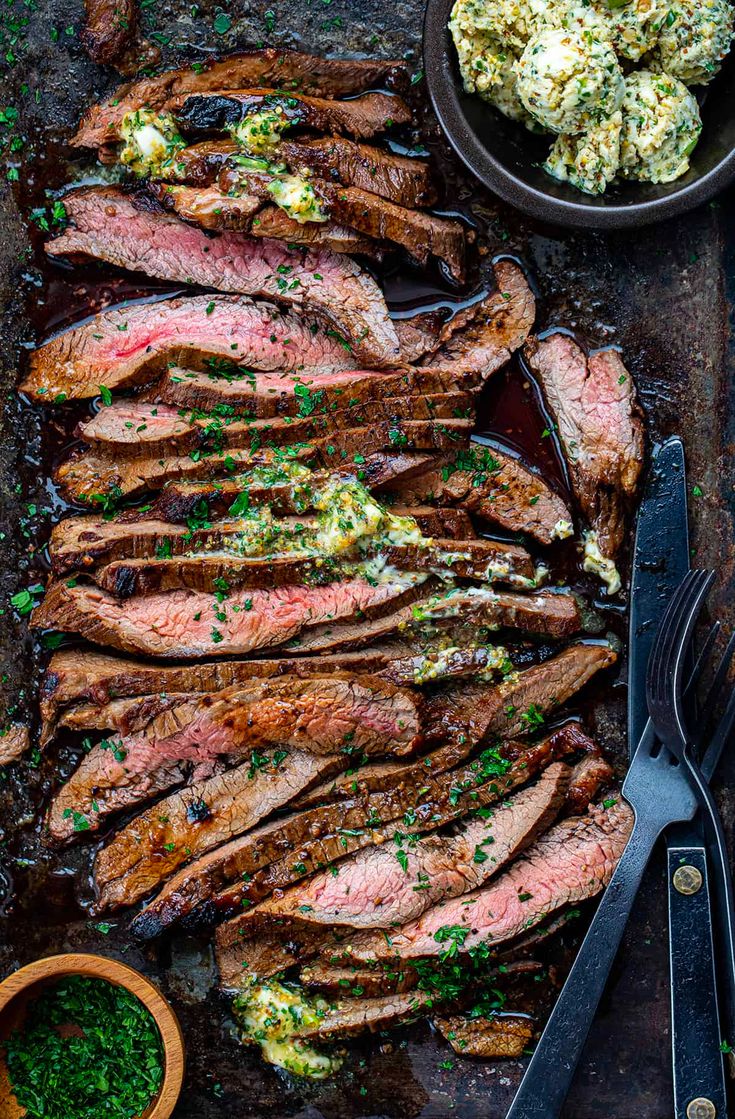 sliced steak with herb butter on the side next to two bowls of salad and utensils