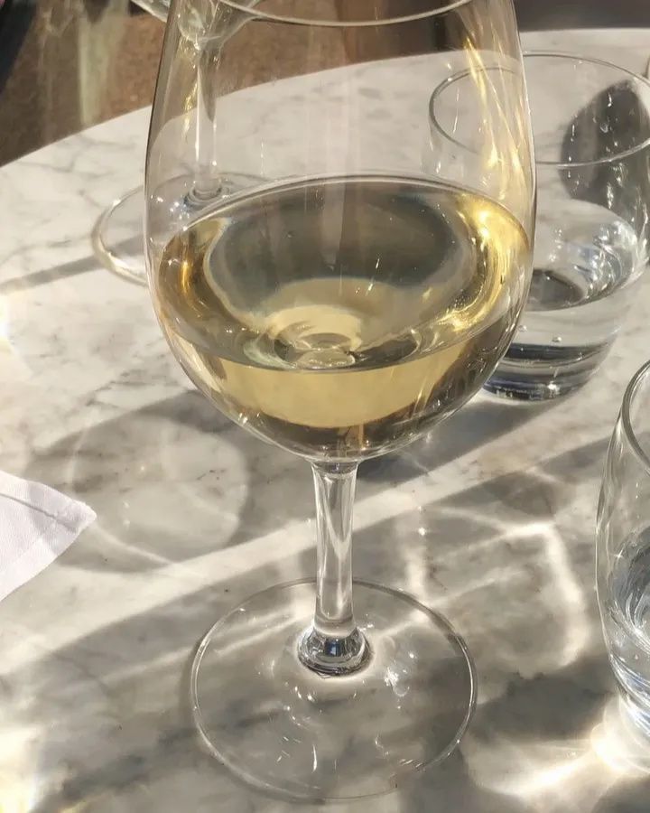 a glass of white wine sitting on top of a table next to two empty glasses