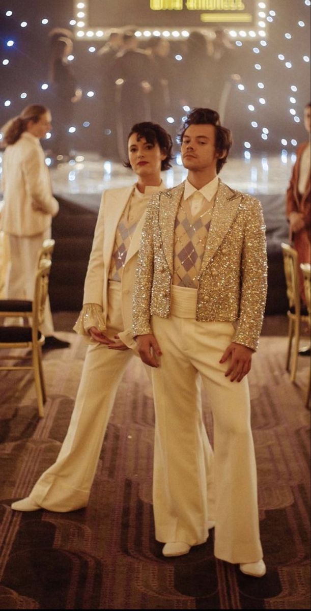 two men in white suits and gold sequins standing next to each other on stage