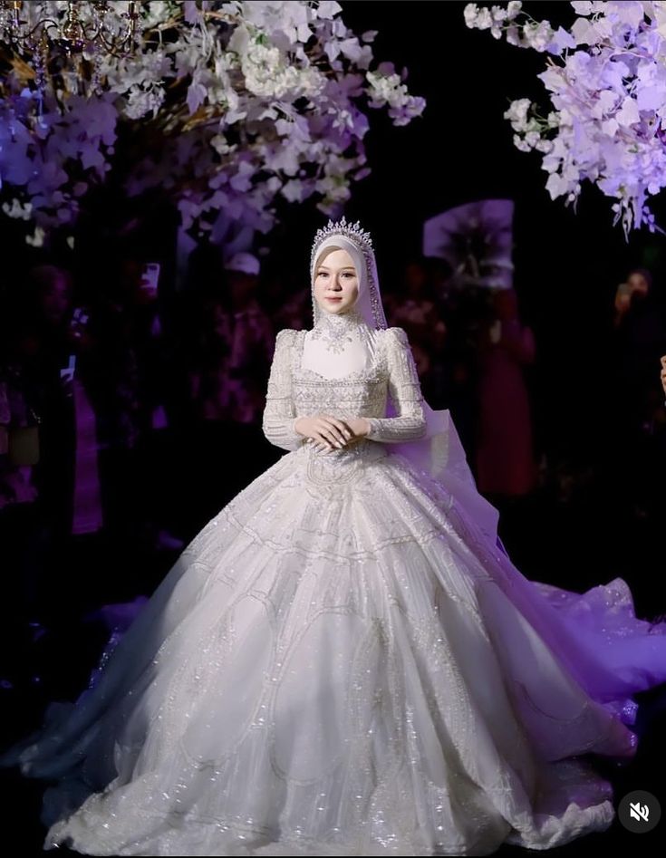 a woman in a white wedding dress standing under a tree filled with purple and white flowers