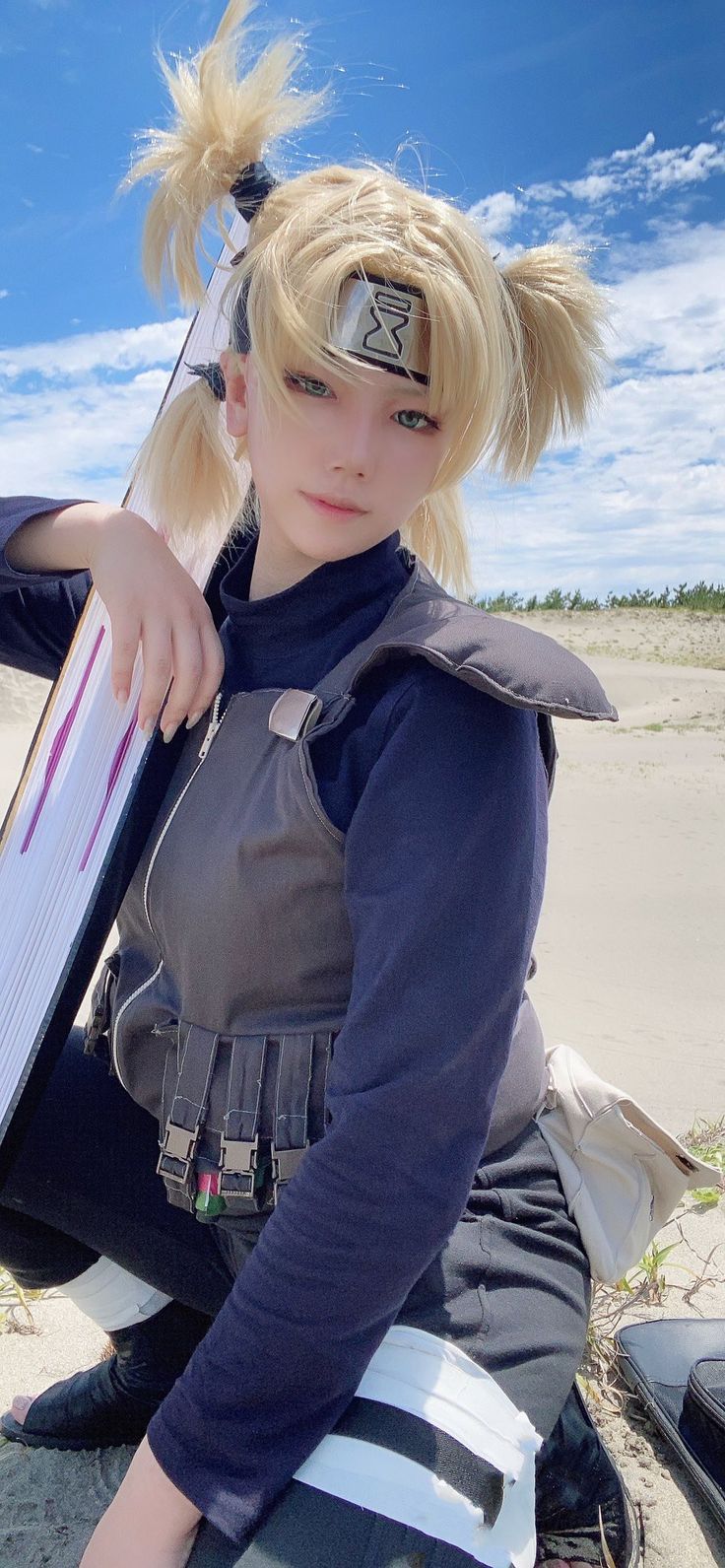 a woman with blonde hair sitting on the ground holding a clipboard and looking at the camera