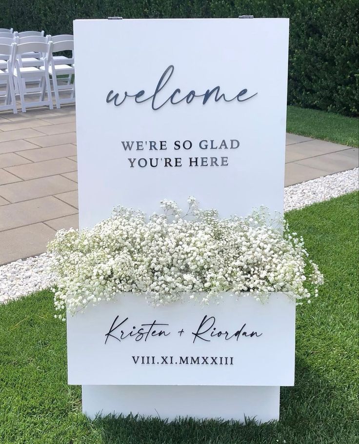 a welcome sign sitting on top of a grass covered field next to a lawn with white chairs