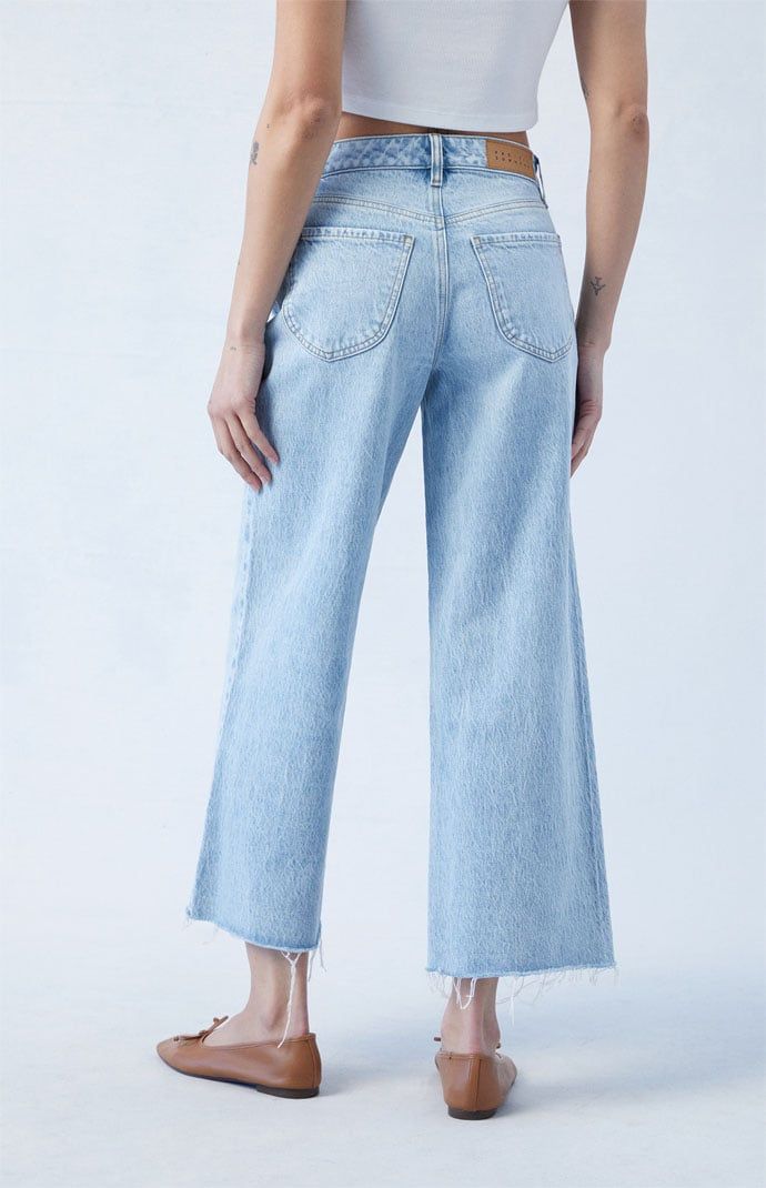 a woman wearing high rise jeans and a cropped tank top, standing in front of a white background