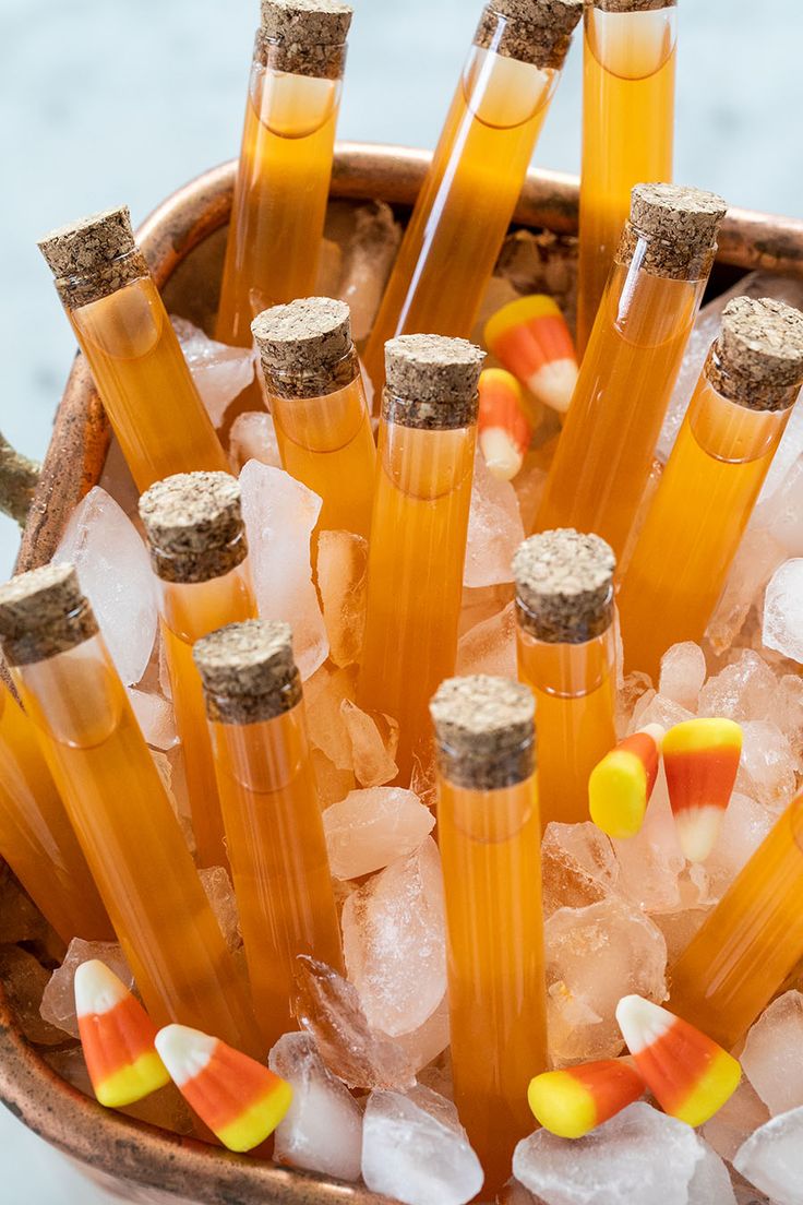 several bottles filled with liquid and candy corn on top of ice cubes in a bowl