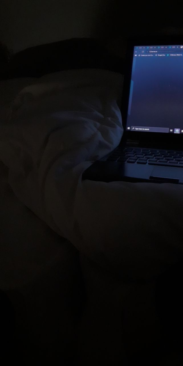 an open laptop computer sitting on top of a bed in the dark with white sheets