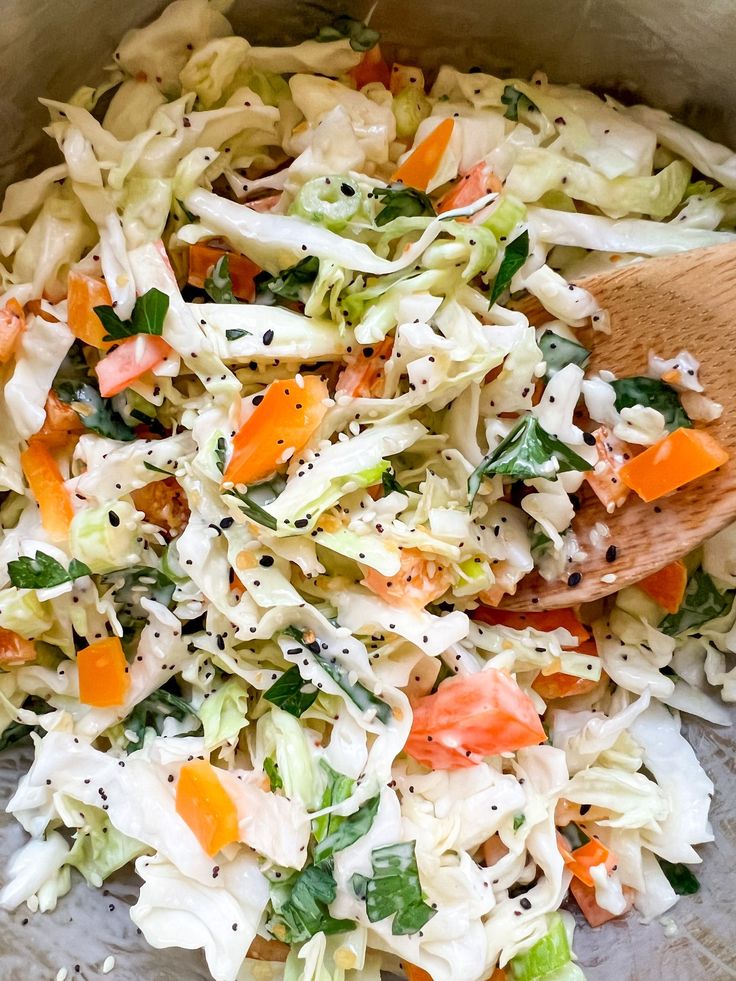 a bowl filled with coleslaw and carrots next to a wooden spoon