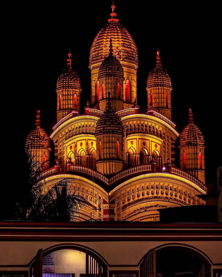 an ornate building lit up at night with red and yellow lights on it's roof