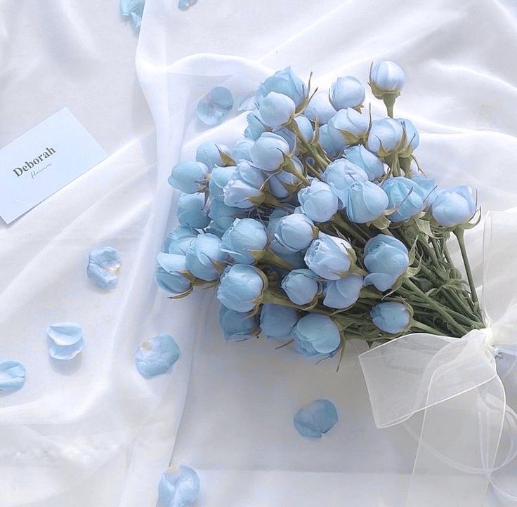 a bouquet of blue flowers on a white sheet with petals scattered around it and a name tag