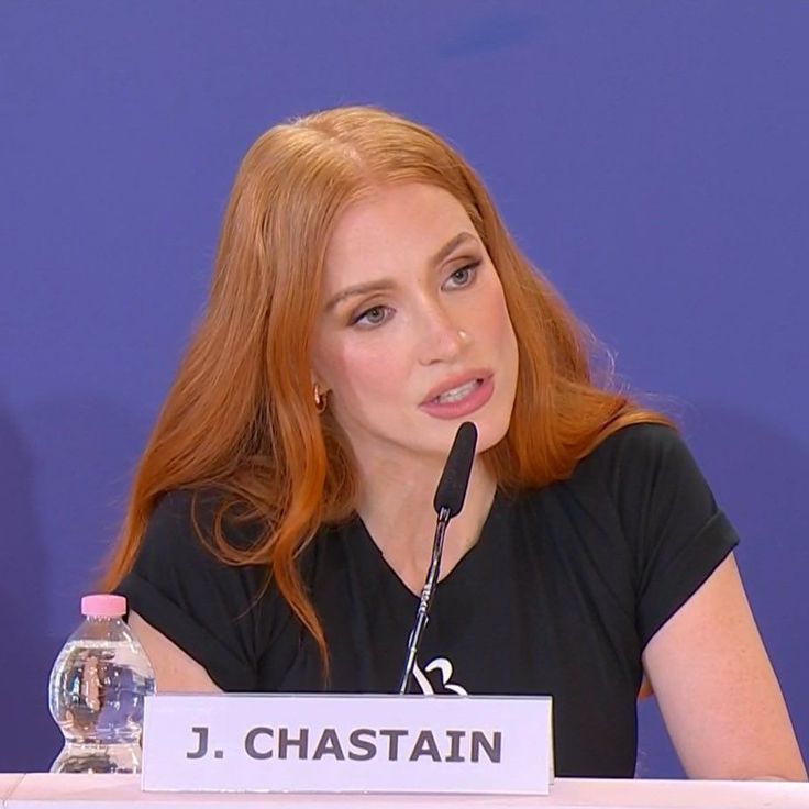 a woman sitting at a table with a microphone in front of her and the words j chastain on it