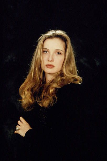 a woman with long blonde hair standing in front of a black background and looking at the camera