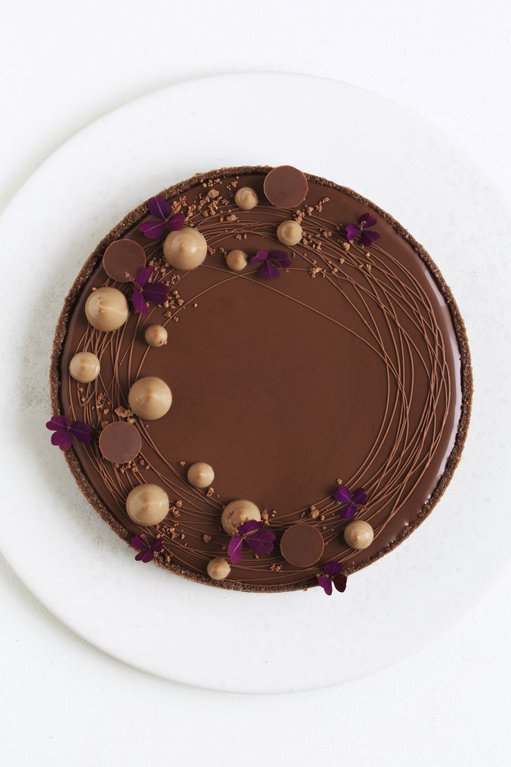 a chocolate cake on a white plate with purple flowers and nuts around the edges, ready to be eaten