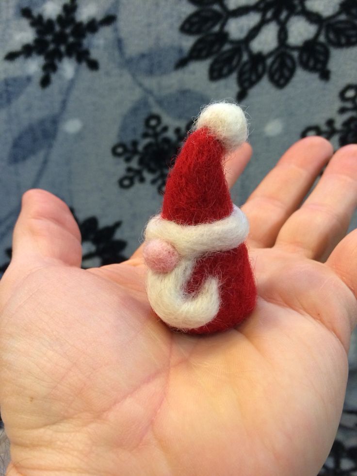 a hand holding a tiny red and white santa hat