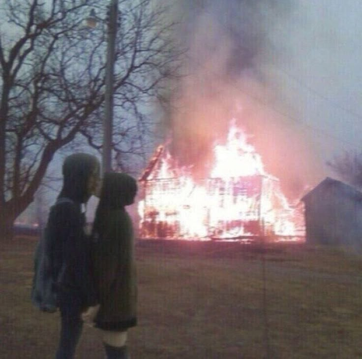 two people standing in front of a house on fire