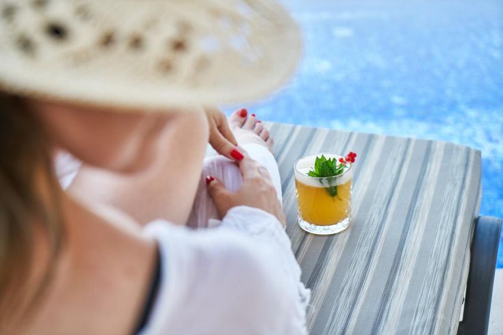 a woman sitting at a table next to a pool with a drink in front of her