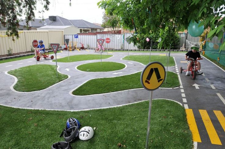 a man riding a bike down a street next to a lush green park filled with children's toys