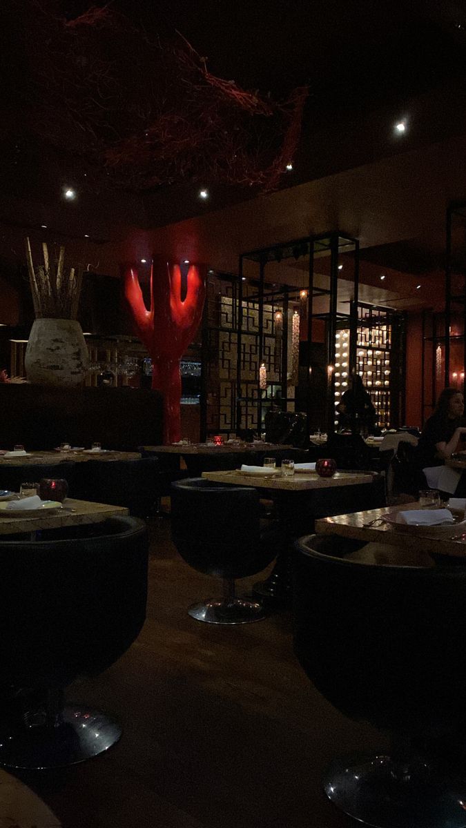 a dimly lit restaurant with many tables and chairs in front of a large red sculpture