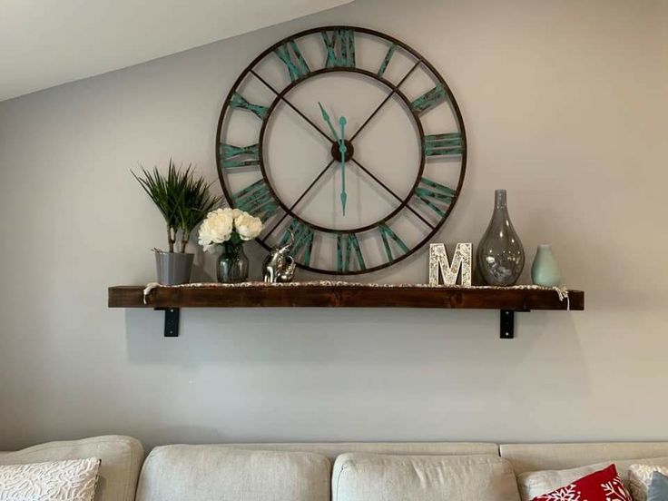 a large clock mounted to the wall above a white couch with pillows and vases on it