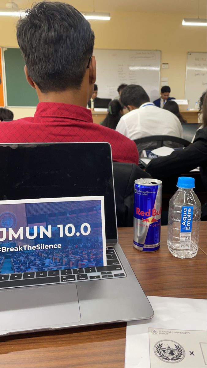 a man sitting in front of a laptop computer on top of a wooden desk next to a bottle of water