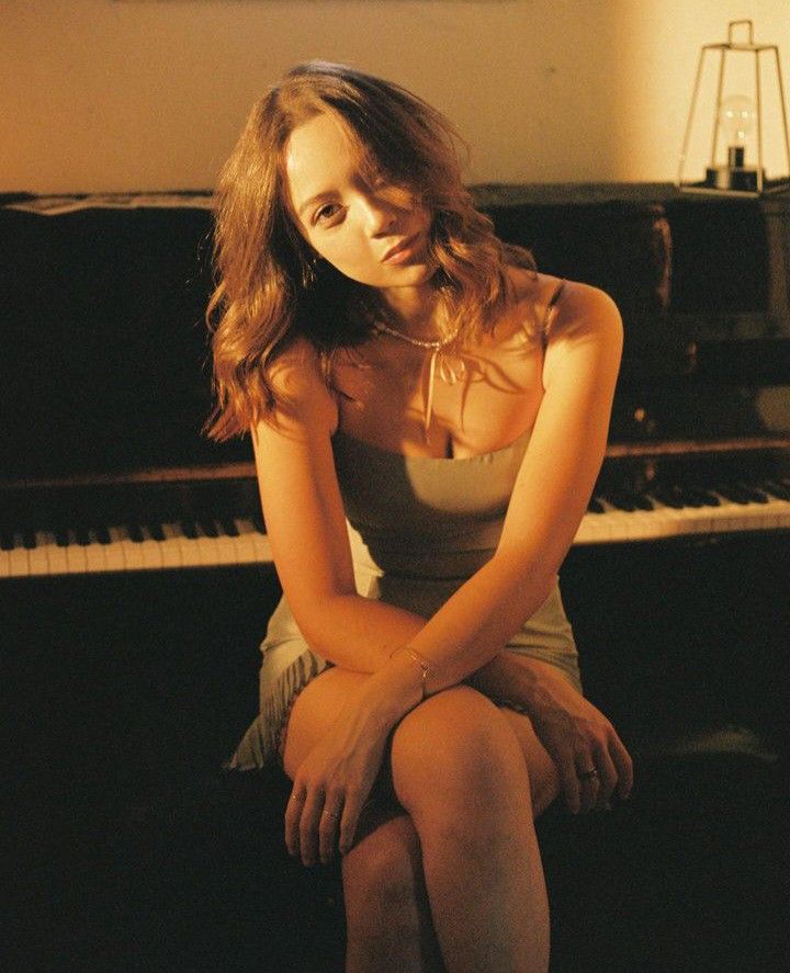 a young woman sitting in front of a piano with her hands on her knees and looking at the camera