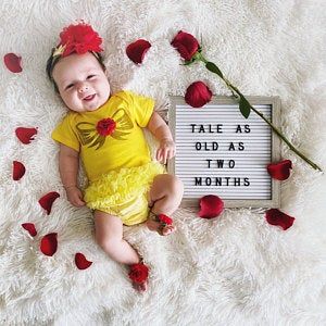 a baby smiles while laying next to a sign that says tale as old as two months