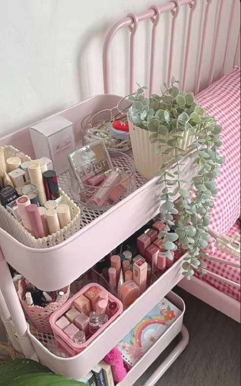 a pink vanity with lots of cosmetics on it and a plant in the corner next to it