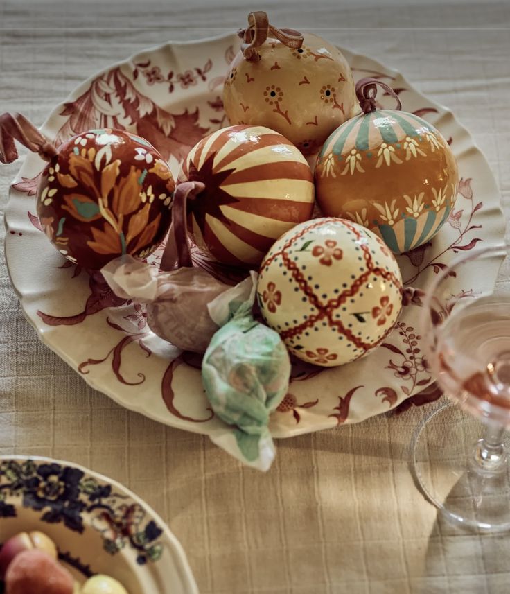 a bowl filled with assorted decorated eggs on top of a table next to wine glasses