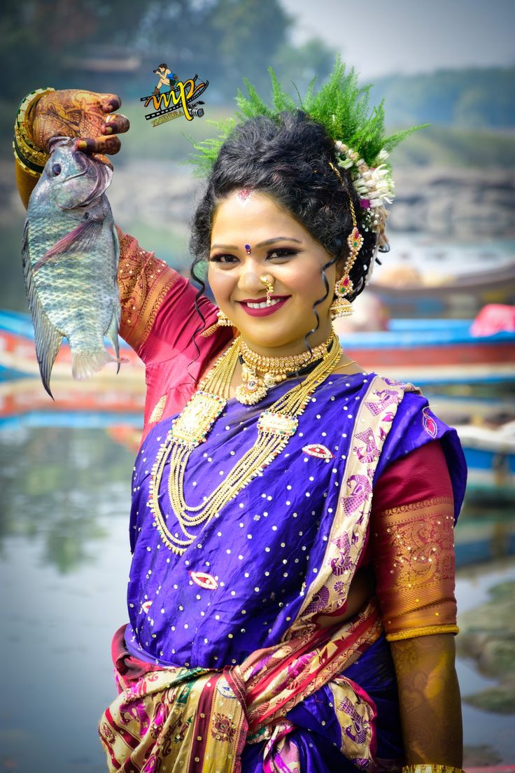 a woman holding a fish in her hand while wearing a purple sari and gold jewelry