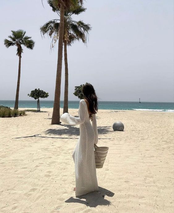 a woman standing on top of a sandy beach next to palm trees and the ocean