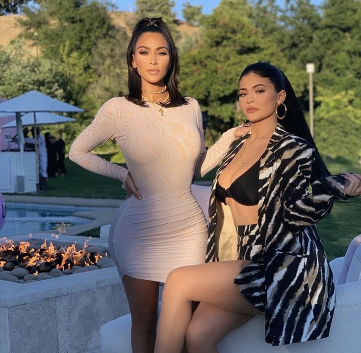 two women posing for the camera in front of a fire pit