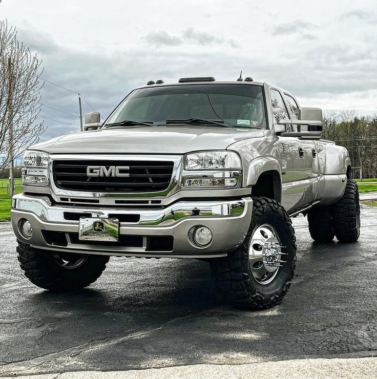 a silver truck parked in a parking lot next to a tree and grass covered field